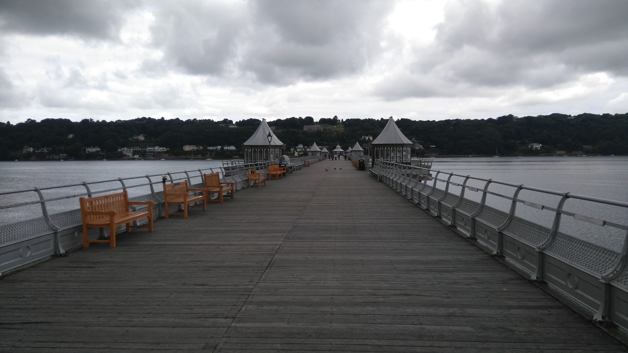 A view down the centre of Bangor Pier in the Menai Strait, Wales, on a cloudy day. Anglesey is in the background.