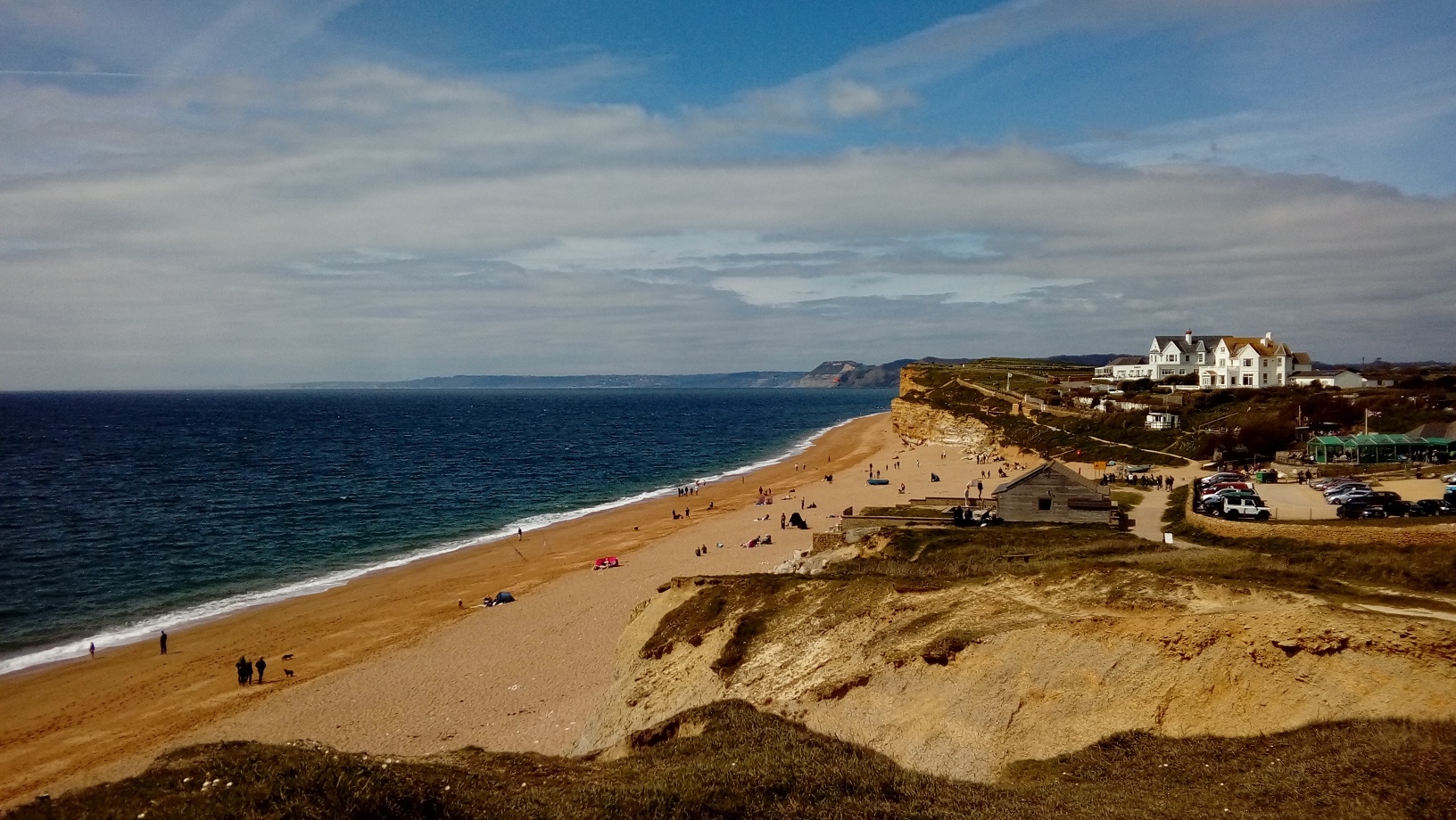 Beach near Burton Bradstock in Dorset viewed on a sunny spring day. Dunes and cliffs are present in the picture, with a distant coastline in the background.