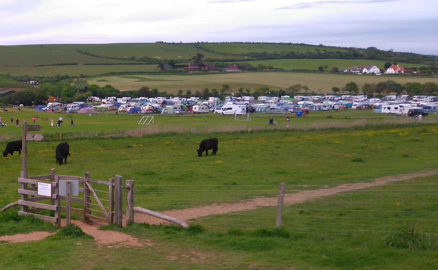A camping site and caravan park at Burton Bradstock in Dorset viewed across rural meadows in a dull summer day. Hills and fields are visible in the background.