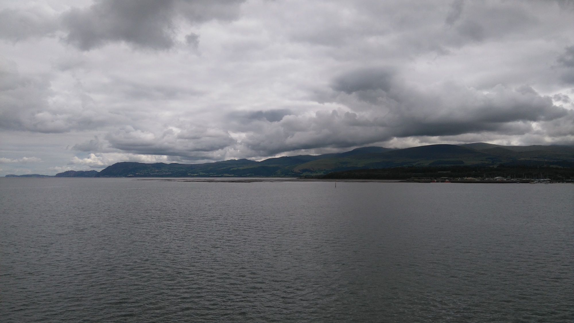 The north Wales coastline on a gloomy summer day, with low clouds hanging over mountains and large hills.