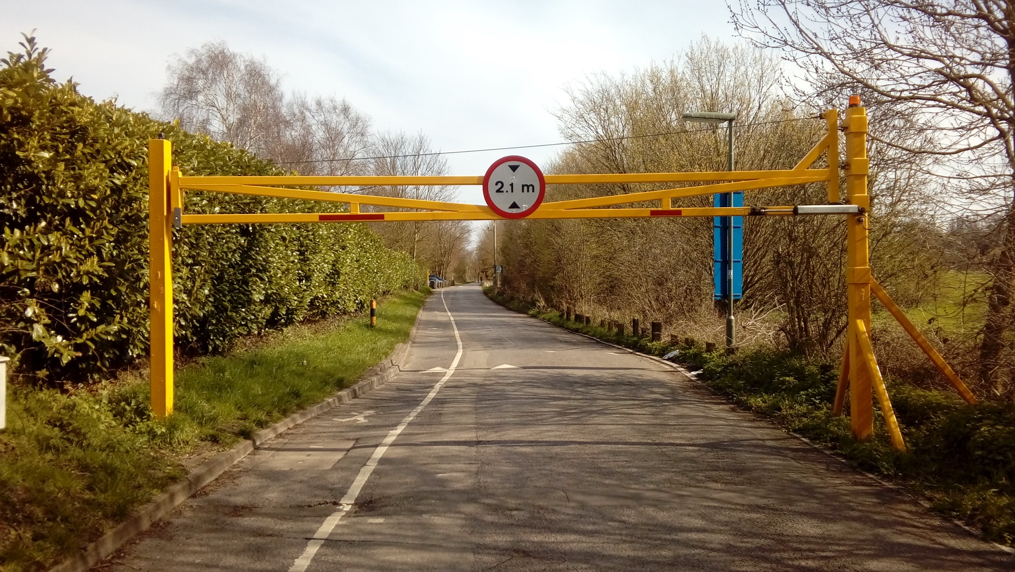A yellow metal height restriction gate placed on a road viewed on a sunny day.