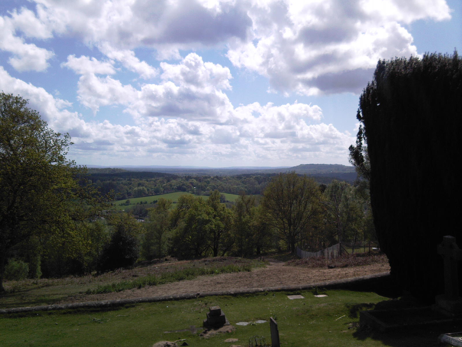 Looking south across the North Downs from a hill top. The view includes trees, hills and woodland under a partly cloudy sky. Taken near Albury, Surrey.