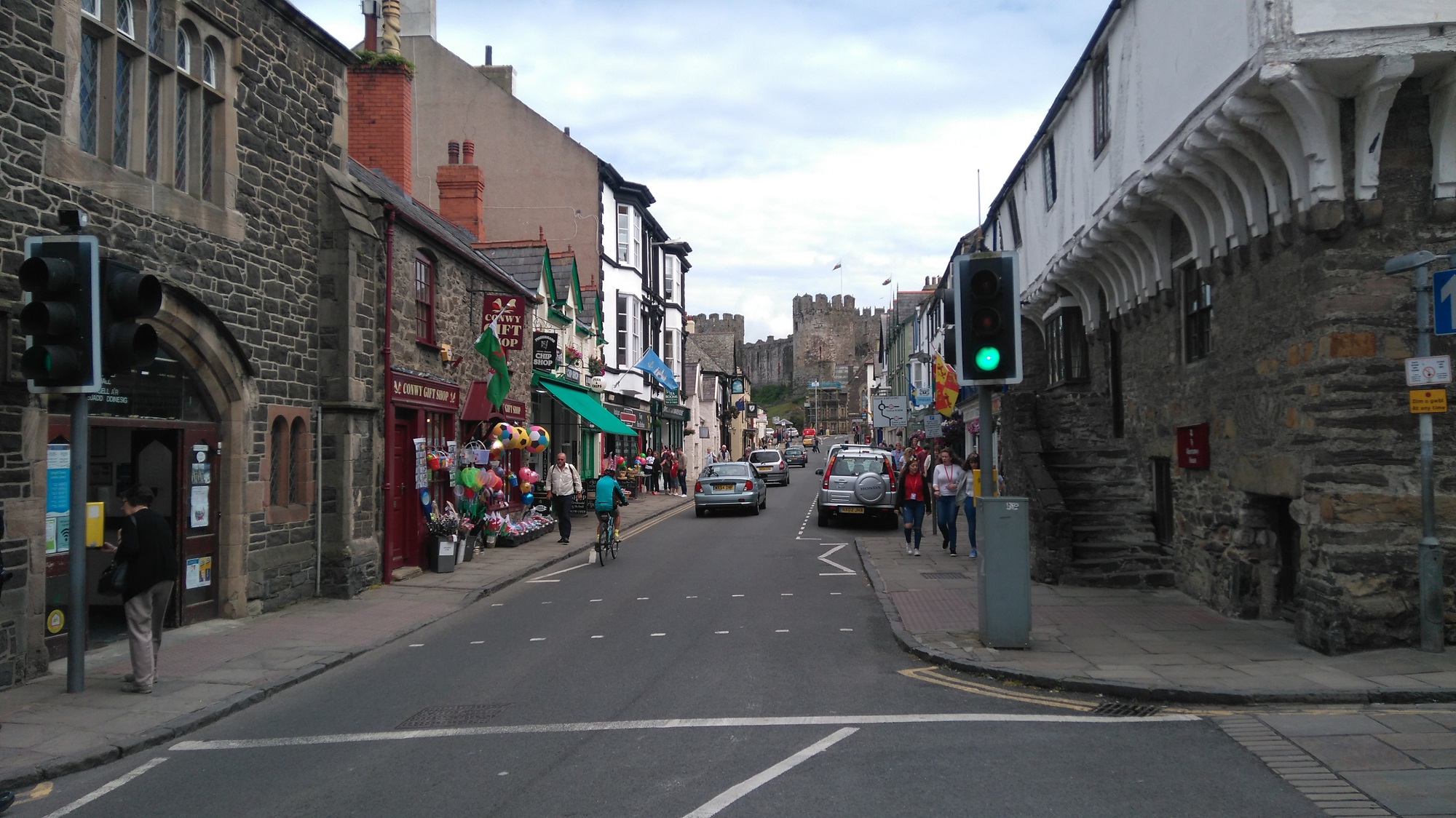 A road junction in the historic Welsh town of Conwy. Picturesque buildings are present, and the castle is visible in the background.