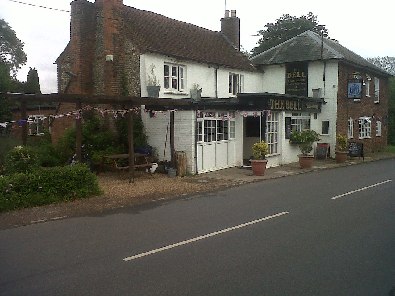 A road side two-building public house with a side garden. A bench and some bunting are present.