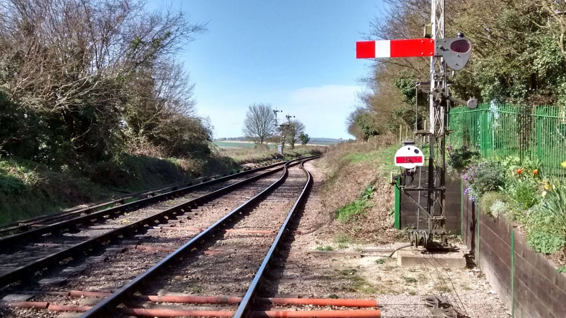 Railway tracks stretch off into the distance under blue sky on a sunny day with a historic signal in the foreground.