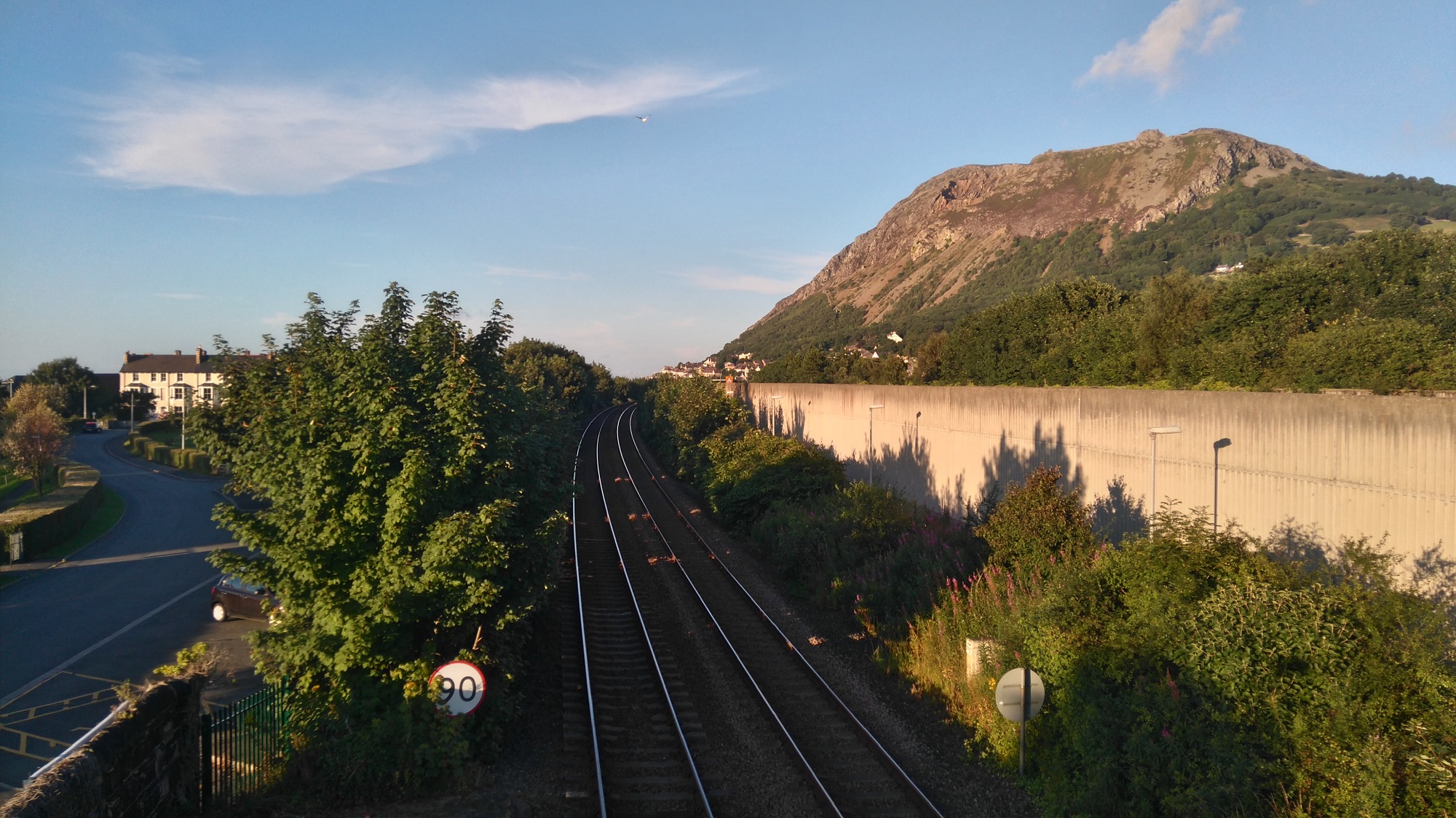Railway tracks stretch into the distance overlooked by a mountain in Wales on a sunny summer evening. Llanfairfechan.
