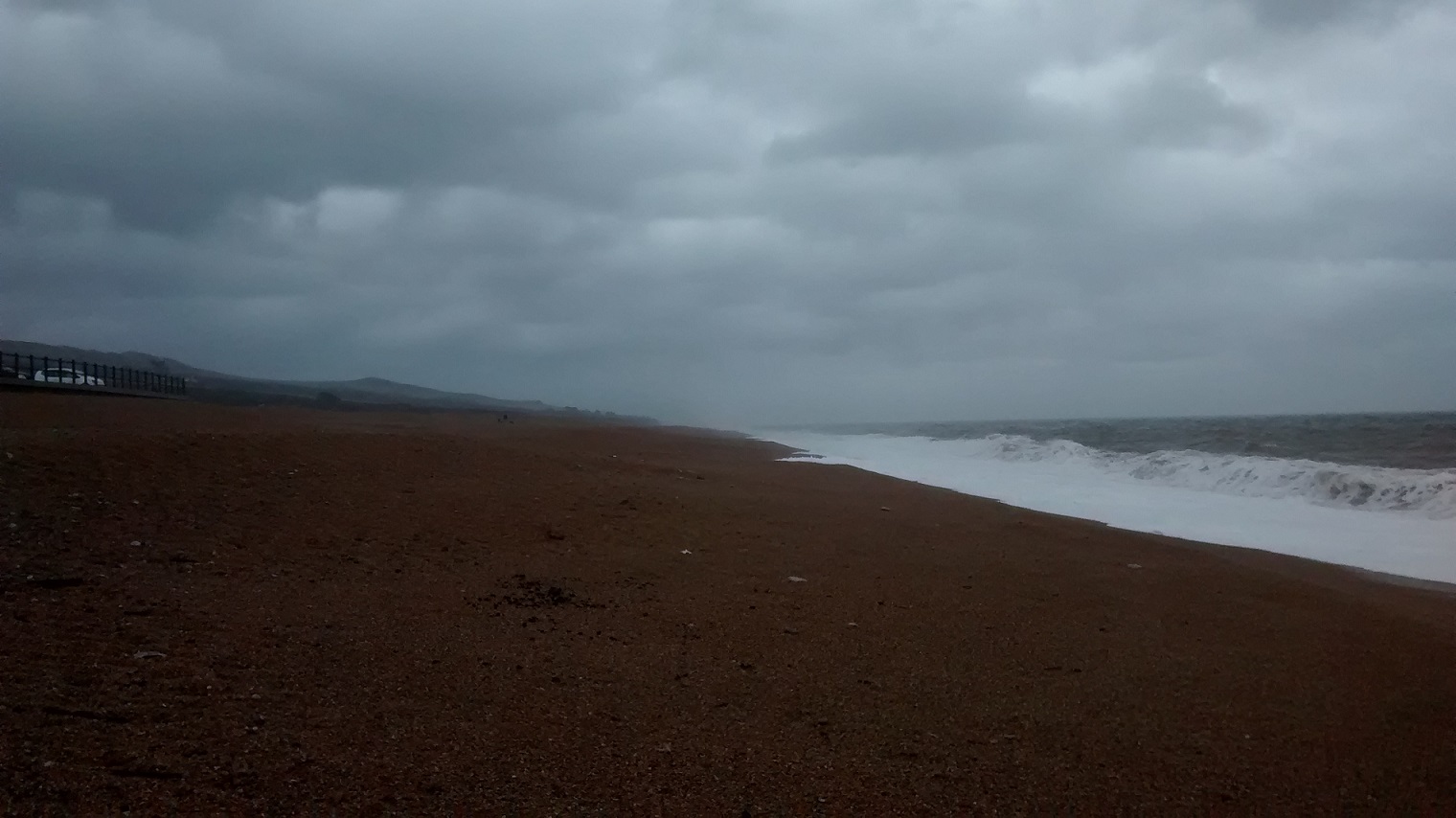 The sea pounds a dark stormy beach under a cloudy sky