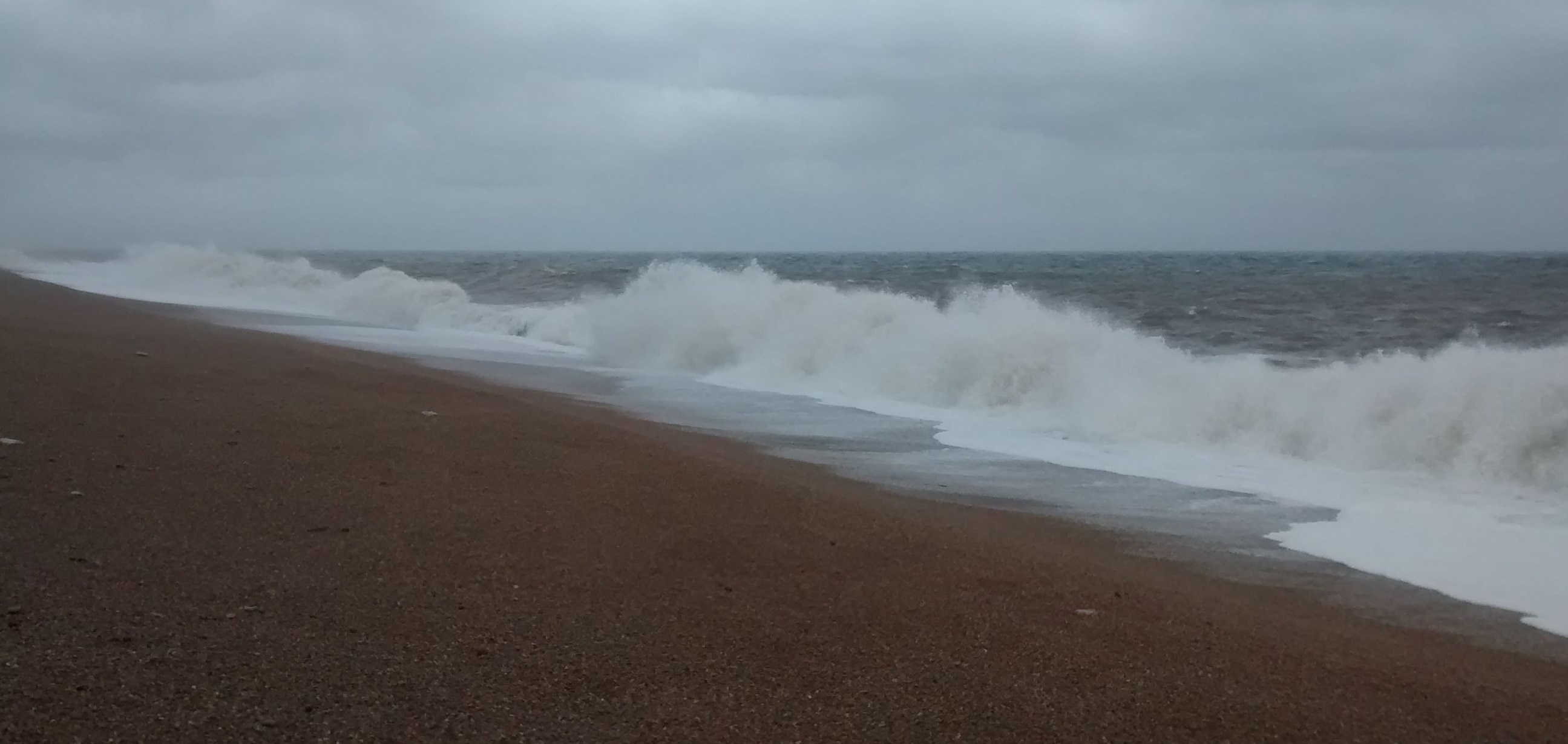 During a storm the sea pounds a pebbled beach under a cloudy sky.