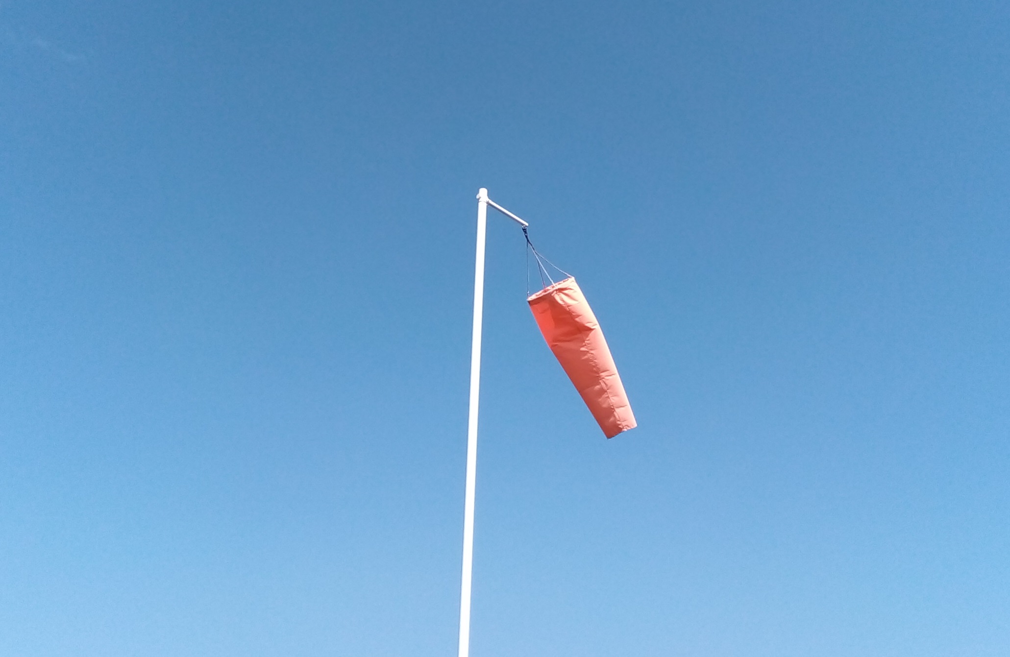 A windsock is viewed on a sunny day against a clear, bright blue sky