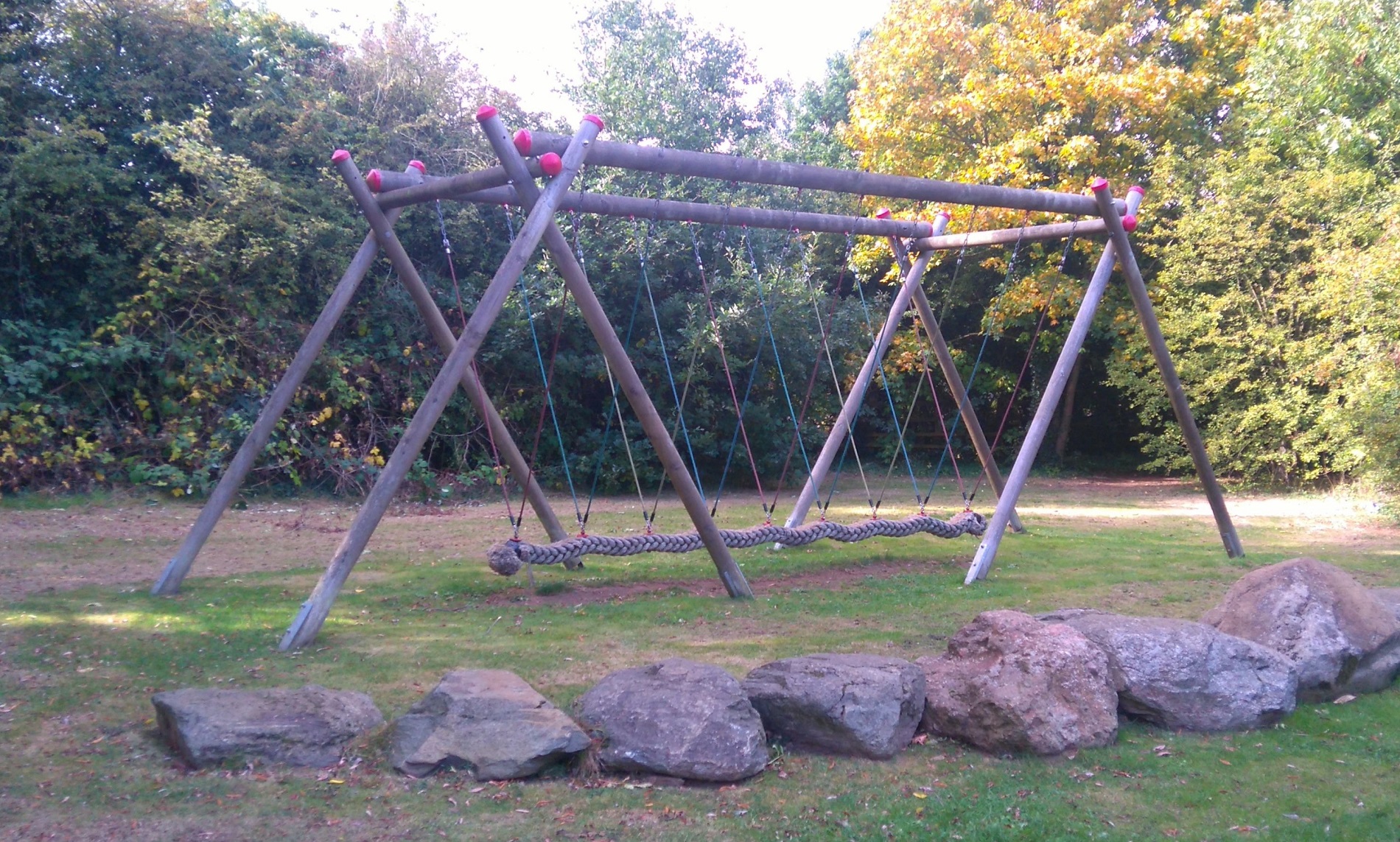 A long swing on a large wooden frame in a playpark, on a bright autumn day.