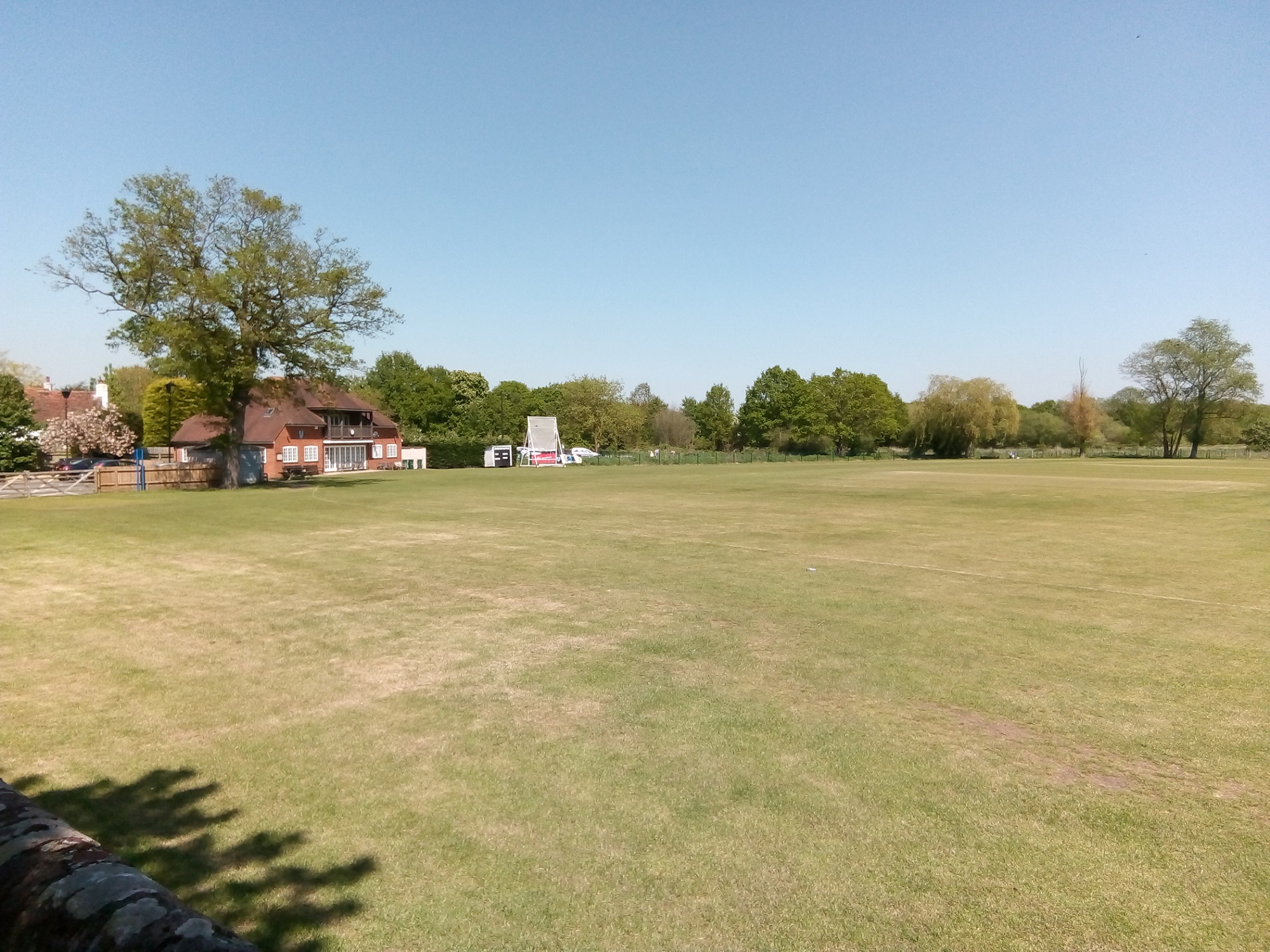 A cricket field and clubhouse in fine sunshine in a rural location.