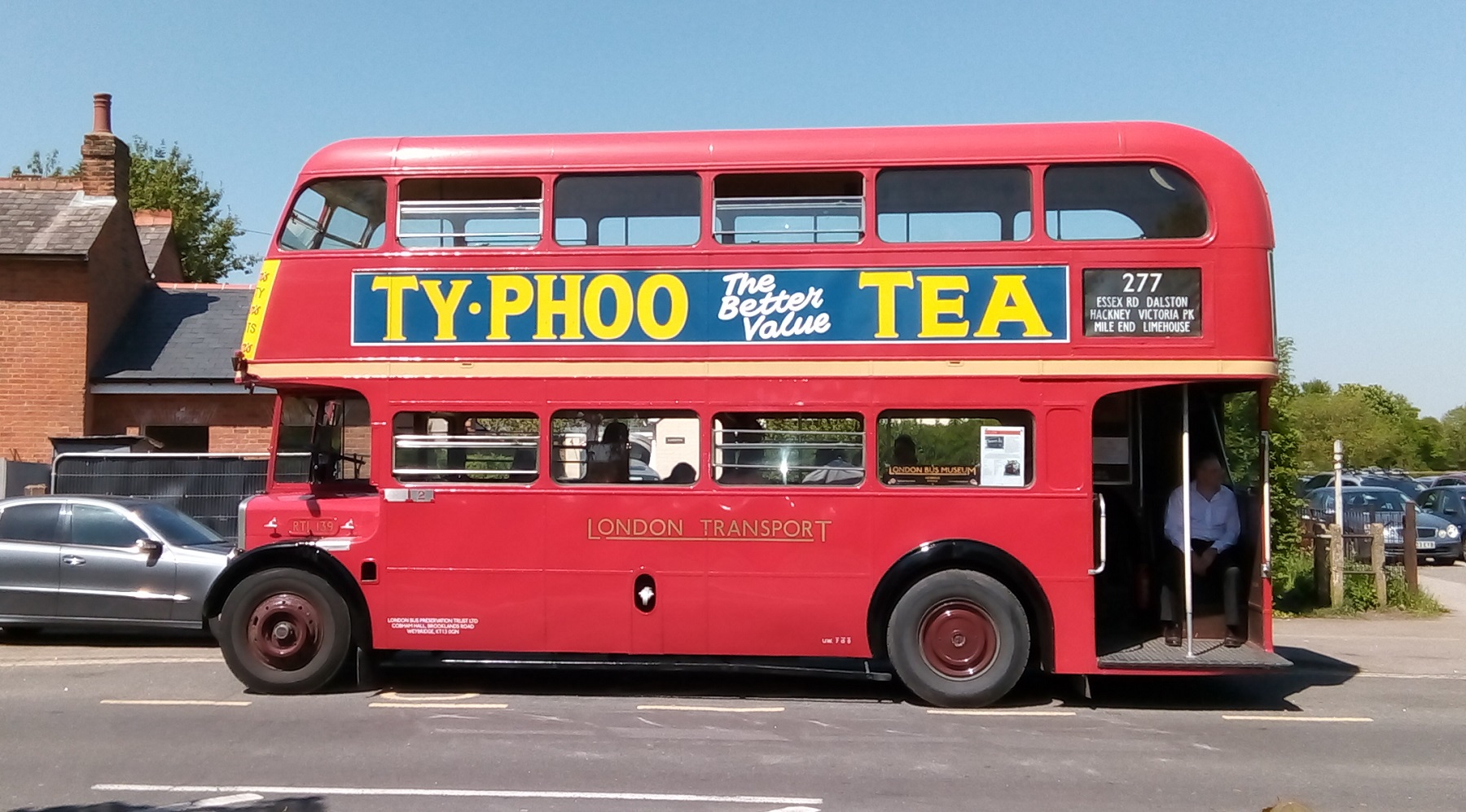 A red London Transport number 277 bus sporting a Typhoo Tea advert parked on a hot sunny day.