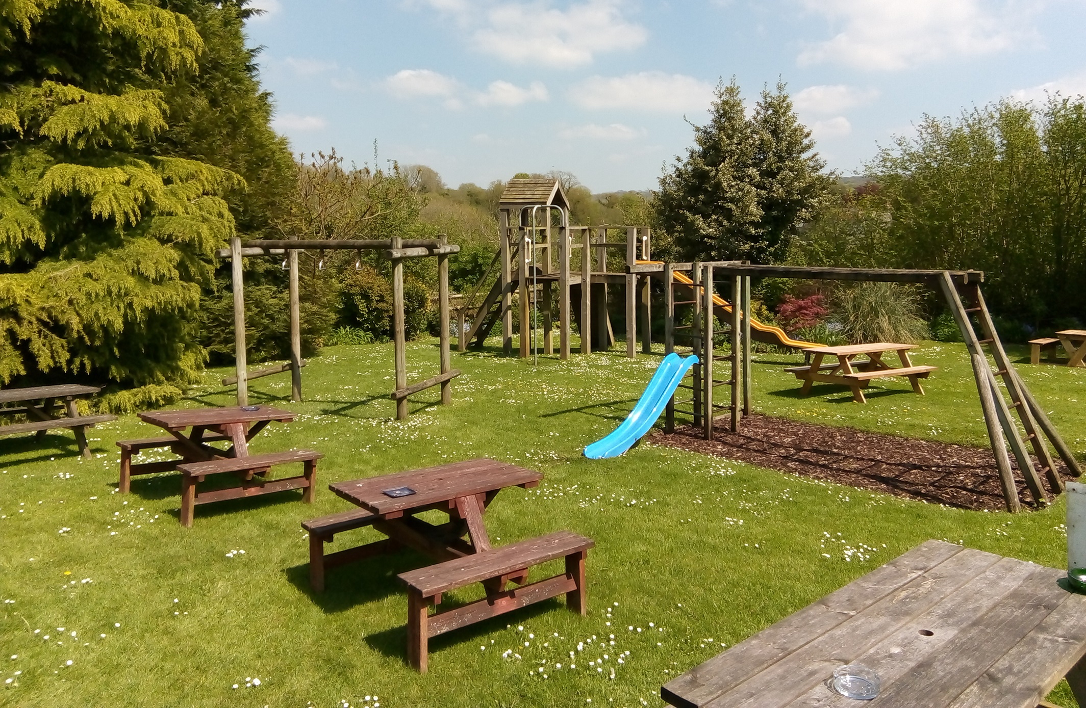 A children's play area in a rural pub garden resplendent with slides and climbing structures, viewed on a sunny day.